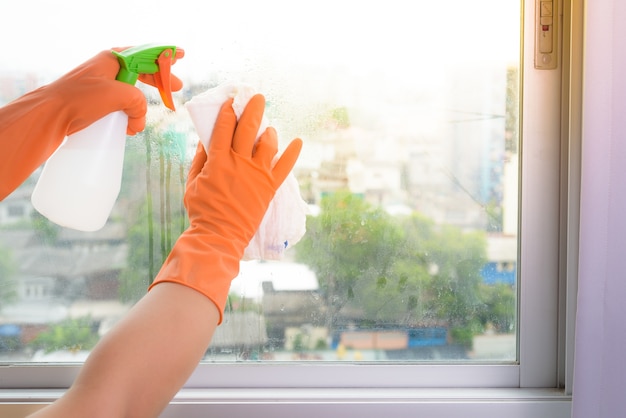 Dien handschoenen in schoonmakend venster met vod en reinigingsmiddelspray thuis.