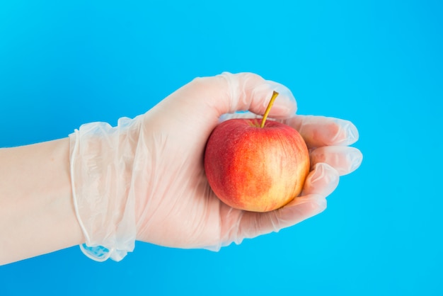 Dien medische handschoen in houdt de rode appel op de blauwe achtergrond. Conceptie van veilige levering