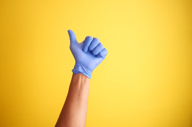 Dien medische handschoenen in die een thumbup tegen gele achtergrond tonen