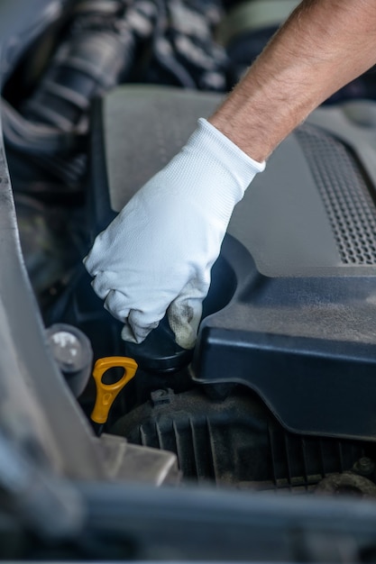 Dien witte beschermende handschoen in die draaiende actie onder open motorkap van auto uitvoert