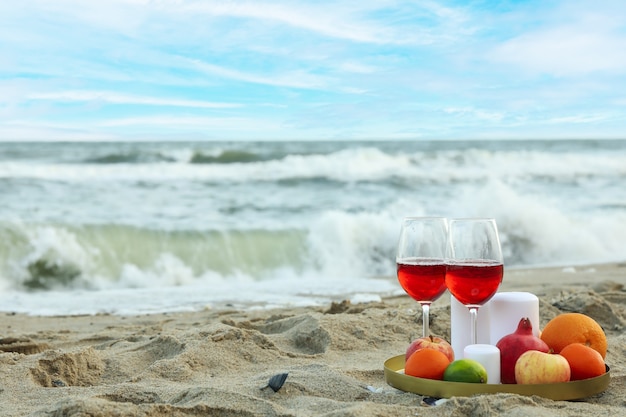 Dienblad met glazen wijn, fruit en kaarsen op zandstrand aan zee