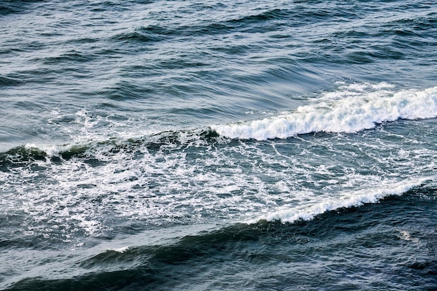 Diepblauwe zeewateren spatten met schuimende golven. Luchtfoto van oceaan spattende golven, donkerblauw golvend zeewater met wit schuim. Wateroppervlak, stormachtige zee. Natuurlijke achtergrond, kopieer ruimte