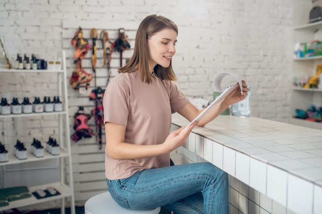 Dierenwinkel. Een meisje in een beige t-shirt zit in een dierenwinkel en kijkt door de prijslijst