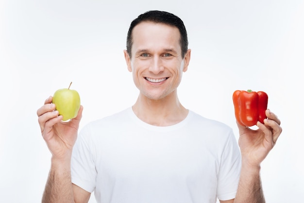 On a diet. Cheerful nice happy msn smiling and looking at you while showing you healthy food