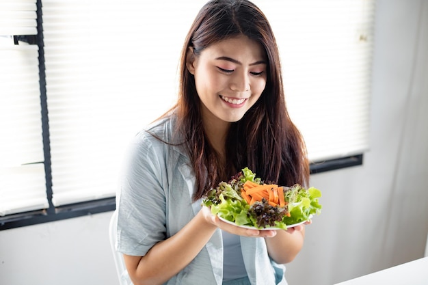 健康的なサラダを食べることによるダイエットの概念。ヘルスケアの笑顔で健康的な食事のための皿野菜を保持している若い女性。