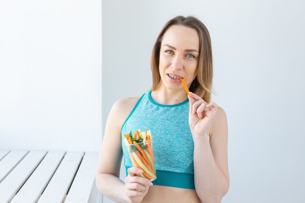 Diet concept - Healthy lifestyle woman eating vegetables smiling happy indoors. Young female eating healthy food.