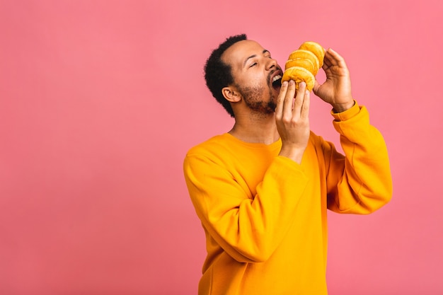 다이어트 개념. 핑크에 고립 된 도넛을 먹는 배고픈 수염 난된 남자.