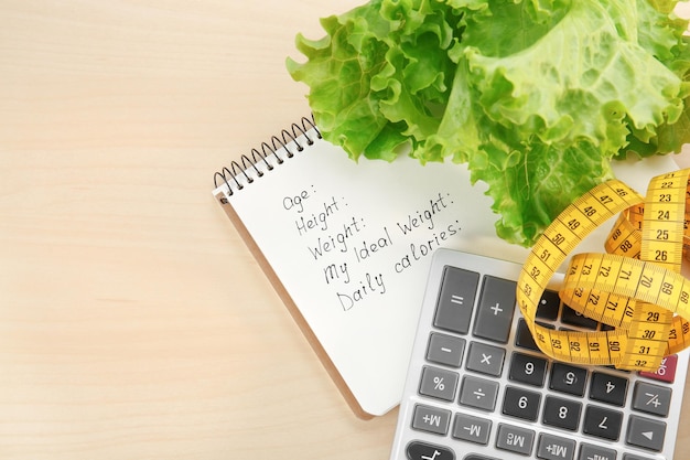 Photo diet concept measuring tape calculator lettuce and notebook on wooden background