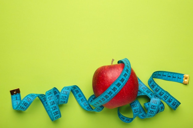 Концепция диеты с яблоком и синей измерительной лентой на зеленом фоне