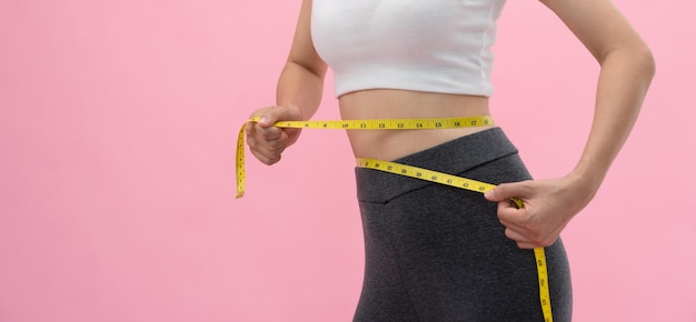 ダイエットとダイエット美しいスリムな女性の体は巻尺を使用します運動服を着た女性は健康的な生活のための減量目標を達成します薄さに夢中細いウエストの栄養士