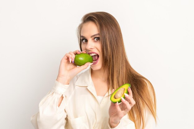 다이어트 영양. 흰색 바탕에 유기농 녹색 아보카도를 물고 있는 아름다운 백인 여성. 건강한 라이프 스타일, 건강 개념입니다.