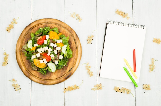 ダイエットは、白い木製のテーブルに新鮮な野菜と白紙のノートのサラダを計画します