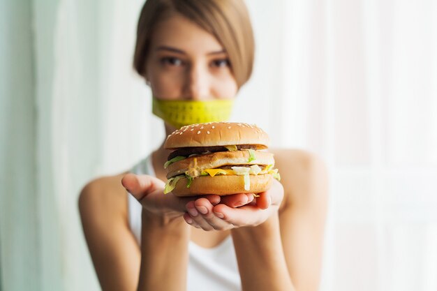 Dieta, ritratto donna vuole mangiare un hamburger ma bloccato bocca skochem, il concetto di dieta, cibo spazzatura, forza di volontà nella nutrizione