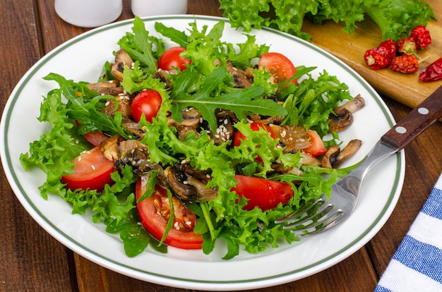 Diet salad of arugula leaves, tomatoes and fried mushrooms on wooden table. Studio Photo.