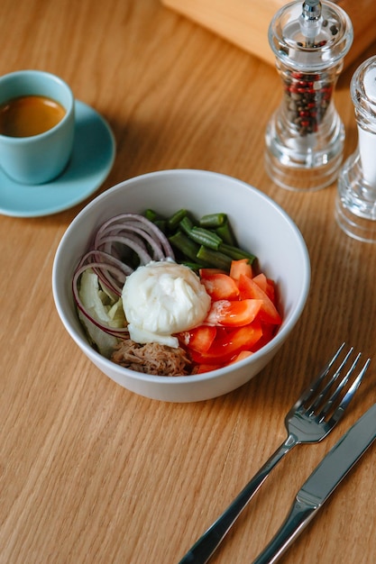 食堂のテーブルの上に立っている新鮮な野菜のダイエットサラダ近くにフォークがあり、コーヒーがあります朝食