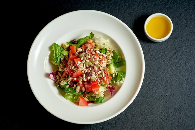 Диетический салат с помидорами и огурцами, семечками в белой тарелке на черном фоне