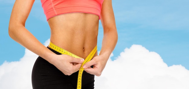 diet, sport, fitness and heath concept - close up of female hands measuring waist with measuring tape