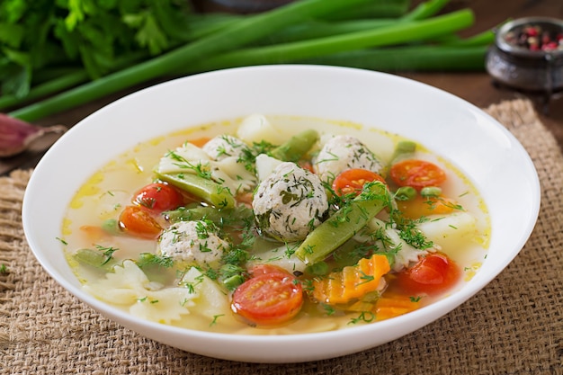 Diet vegetable soup with chicken meatballs and fresh herbs in wooden bowl