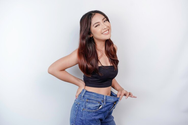 Photo ダイエットと減量のコンセプト白い背景に特大のジーンズを着た若いアジア人女性