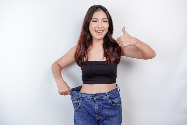 Photo ダイエットと減量のコンセプト白い背景に特大のジーンズを着た若いアジア人女性