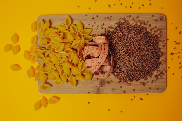 Diet and weight loss theme. Buckwheat, macaroni products and measuring tape on the wooden cutting board. Slow carbohydrates.