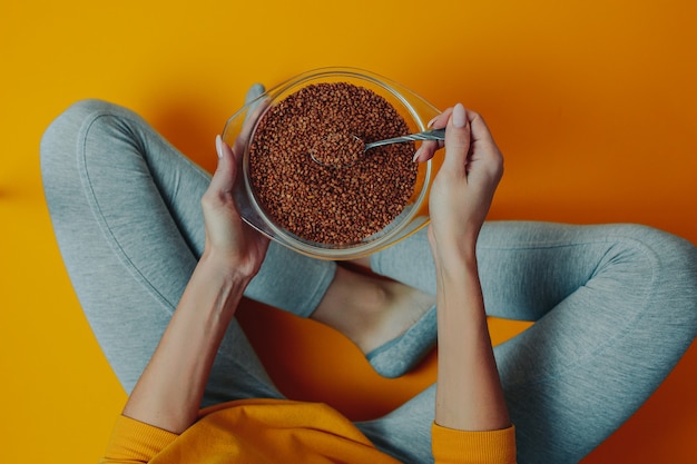 Diet and weight loss theme. Woman holds buckwheat in the plate and spoon. Woman on diet.