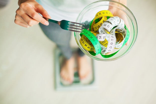 Diet and Weight Loss. Woman holds bowl and fork with measuring tape.