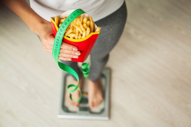 Рацион питания. Женщина, стоящая на весах и держащая картофельные чипсы.