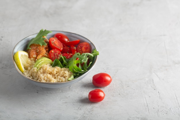 Dietary bowl salad with quinoa, salmon and vegetables, such as tomatoes and arugula. Fresh vitamin organic salad.