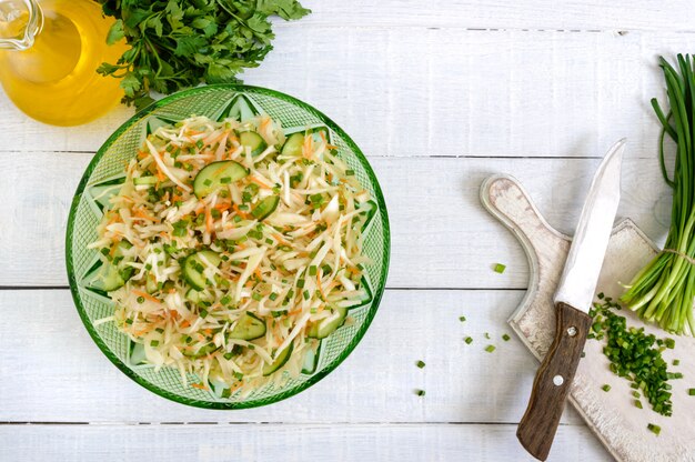 Photo dietary salad with cabbage, cucumber, carrot, greens. juicy spring salad from fresh vegetables on a white wooden background. proper nutrition. the top view