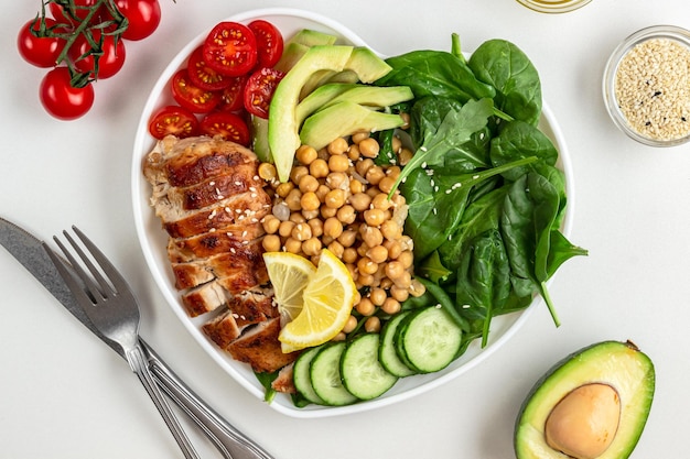 Foto insalata dietetica con pollo avocado cetriolo pomodoro e spinaci su sfondo bianco posa piatta