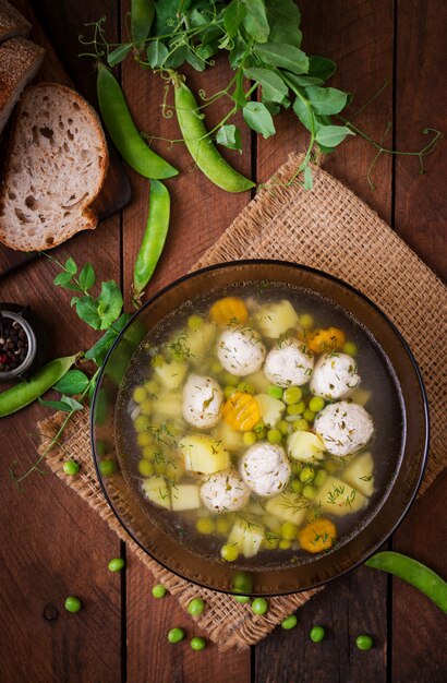 Dietary soup with chicken meatballs and green peas in a glass bowl on a wooden table.