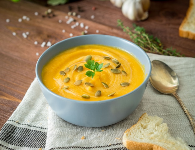 Dietary vegetarian pupmkin cream soup puree,  on dark brown wooden table, side view, close up.