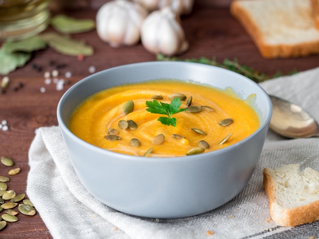 Dietary vegetarian pupmkin cream soup puree,  on dark brown wooden table, side view, close up.