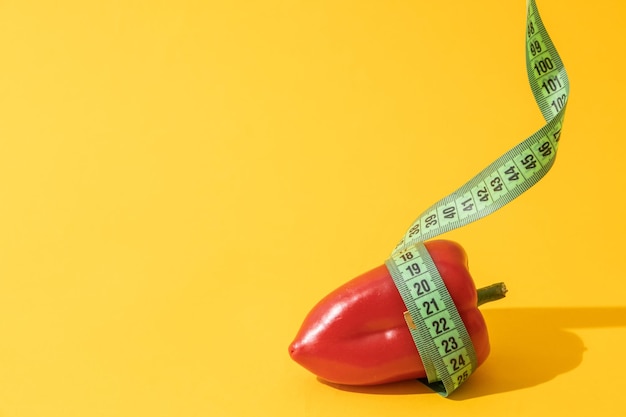 Dieting concept sweet bell pepper is wrapped with green measuring tape on yellow background