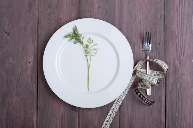 Dieting concept white plate with dill fork and centimeter tape