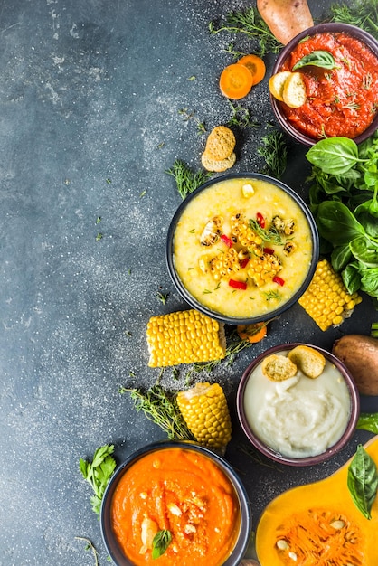 Different autumn soups set Assortment vegetable soups in portion bowls corn potato pumpkin tomato zucchini broccoli cream soups On black concrete background top view copy space