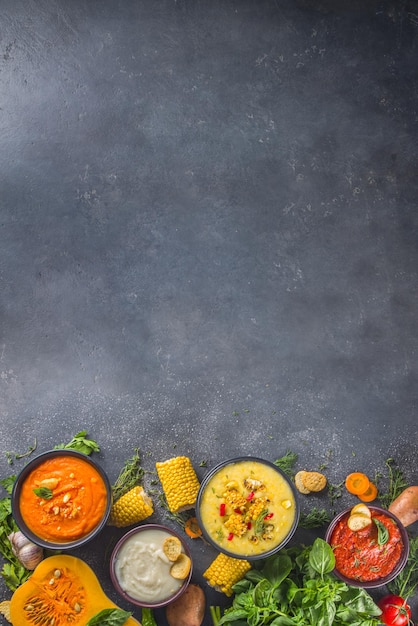 Photo different autumn soups set assortment vegetable soups in portion bowls corn potato pumpkin tomato zucchini broccoli cream soups on black concrete background top view copy space