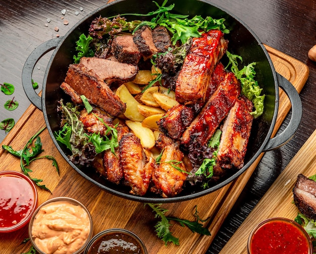 Different barbecue meat with potatoes in a frying pan