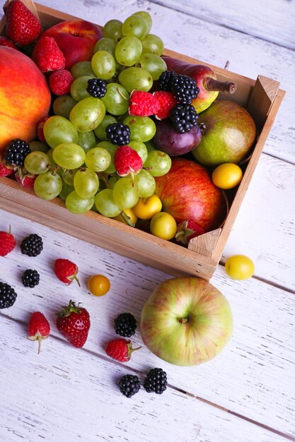 Different berries and fruits in box on wooden table closeup