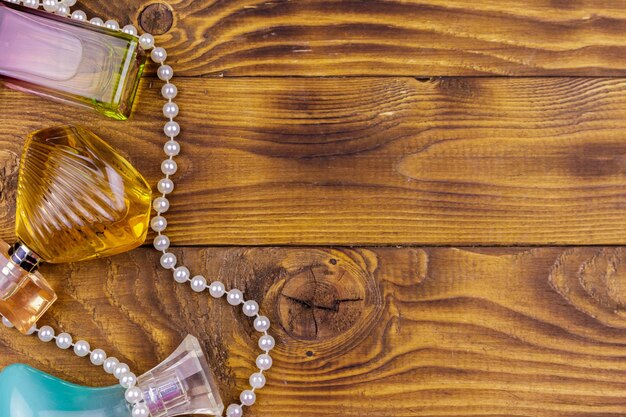 Different bottles of perfume and pearl necklace on wooden background Top view copy space