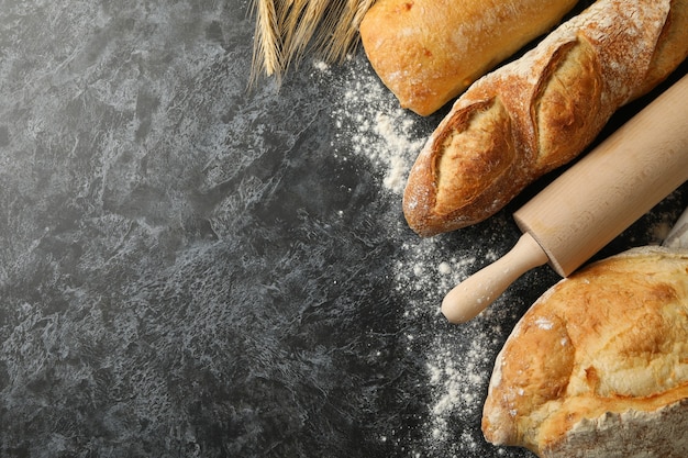 Different bread, spikelets and rolling pin on black smokey background