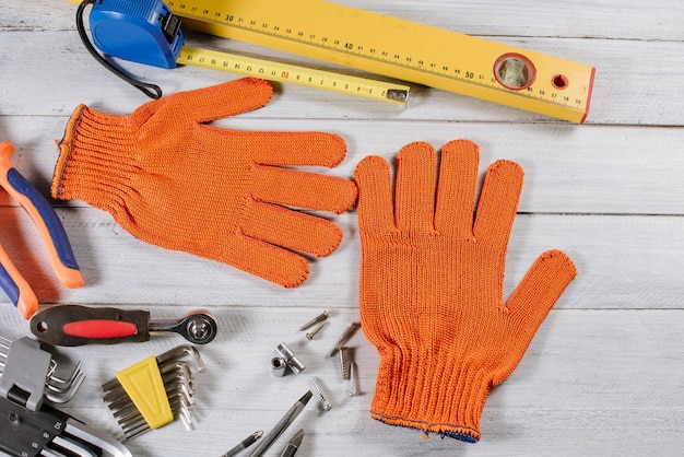 Different building or crafting tools and gloves flatlay on white wooden background