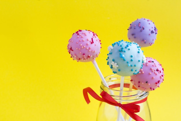 Different cake pops in the glass jar on the yellow surface