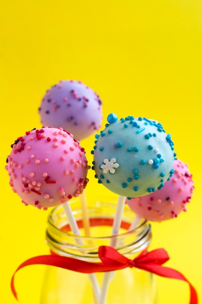 Photo different cake pops in the glass jar on yellow