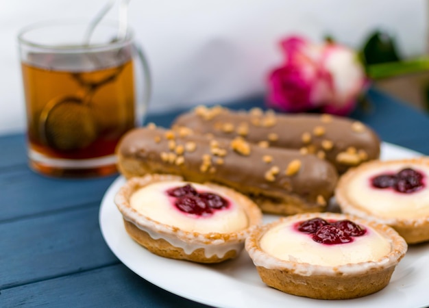 Different cakes with custard and cream and berries on a white plate with tea in the background