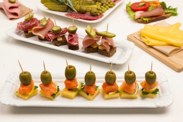 Different canapes with salmon, cucumber, tomatoes, cheese, meat on white background