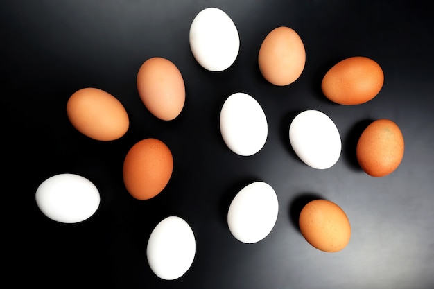 Different chicken eggs lie on dark background