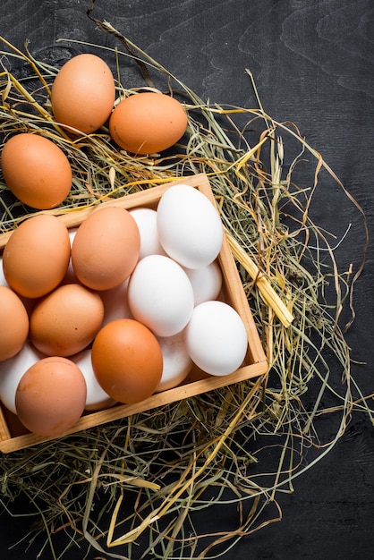 Different chicken eggs in wooden box on black background. Copy space