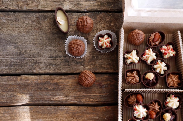Различные шоколадные конфеты в бумажной коробке на деревянном фоне, крупным планом
